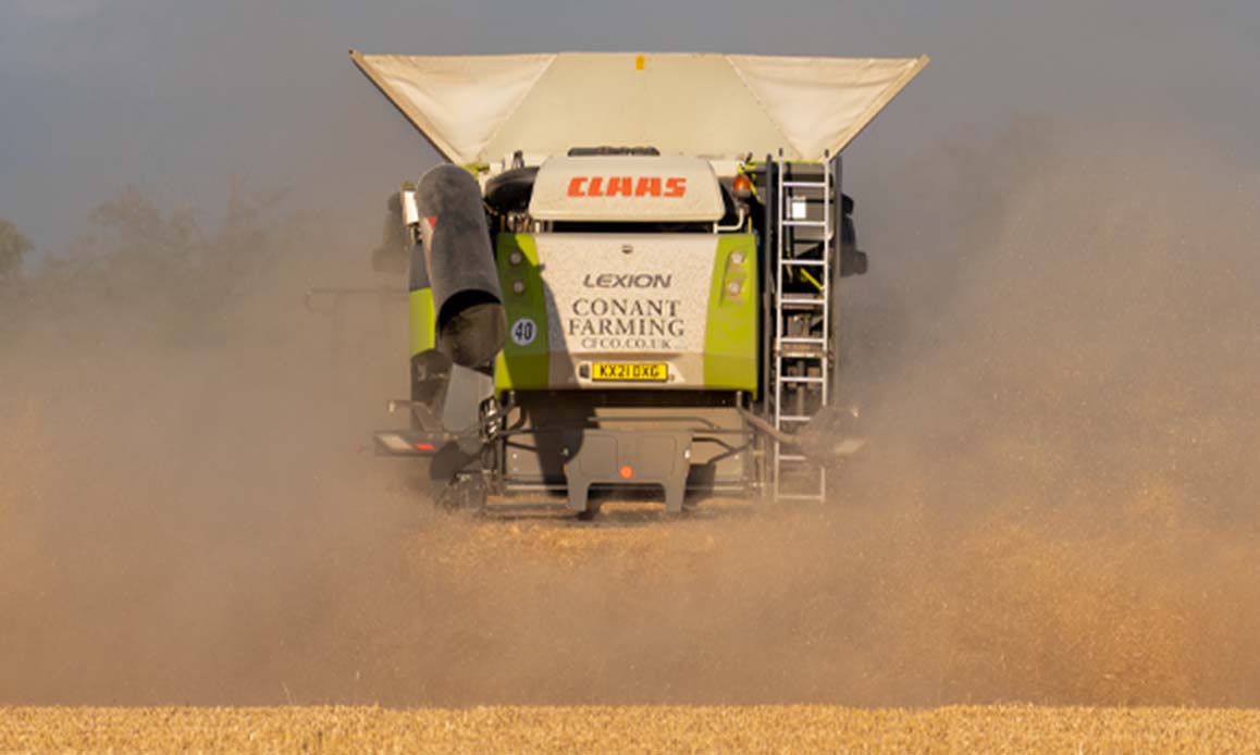 Claas Lexion combine disappearing into the dust leaving a trimmed stubble carpet in its wake.